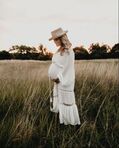 Pregnant woman standing in a field gently holding her belly
